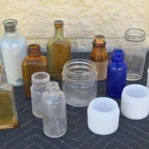 Collection of vintage glass bottles and jars in various shapes, sizes, and colors, including amber, cobalt blue, clear, and milk glass.