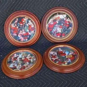 Set of four vintage Coca-Cola Santa Claus collector plates, each housed in a round wooden frame.