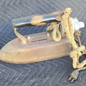 Vintage electric flat iron with a worn wooden handle and a heavily frayed fabric-covered power cord, showing significant rust and age.
