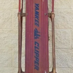 Vintage Yankee Clipper wooden snow sled with red painted deck and metal runners, showing moderate wear from age and use.