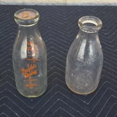 Two vintage glass milk bottles, including one featuring orange pyroglazed lettering for People's Dairy of Lake Placid, New York.