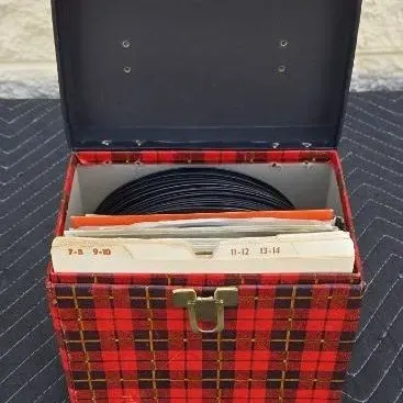 Vintage red and black plaid 45 RPM record carrying case, filled with vinyl records and index dividers.