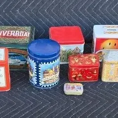 Collection of vintage decorative metal tins in various shapes, sizes, and colorful designs, showing some light wear consistent with age.