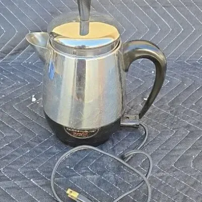 Vintage Farberware Super Fast electric coffee percolator with a stainless steel body, black plastic handle, and power cord.