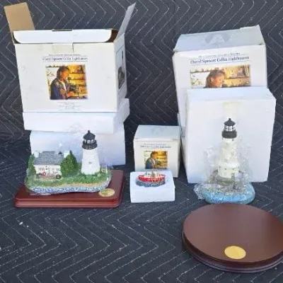 Collection of Cheryl Spencer Collin lighthouse figurines, some in original packaging with wooden display bases.