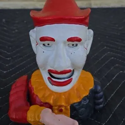 Vintage cast iron mechanical clown bank, featuring a hand that moves to place a coin in the mouth, with some paint wear consistent with age.