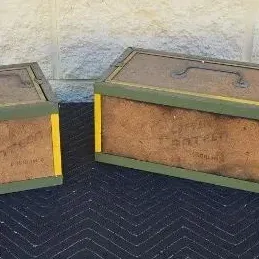 Two vintage wooden and metal storage crates with green and yellow trim, featuring metal handles and stenciled lettering on the sides.