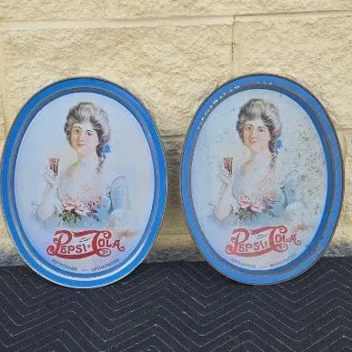 Pair of vintage oval Pepsi-Cola metal serving trays featuring a classic illustration of a woman holding a glass, showing some wear and...
