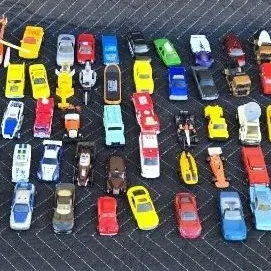 Large collection of vintage and modern die-cast toy cars, including Hot Wheels and Matchbox models, displayed on a dark quilted mat.