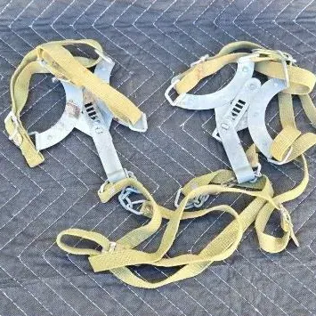 Vintage military-style ice crampons with adjustable metal frames and canvas webbing straps, showing some age-related wear.