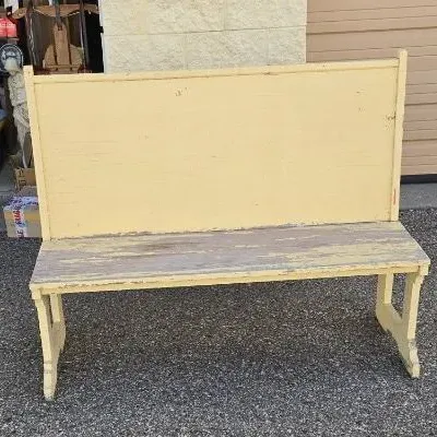 Rustic wooden high-back bench with a distressed yellow painted finish and worn seat, showing a charming weathered patina.