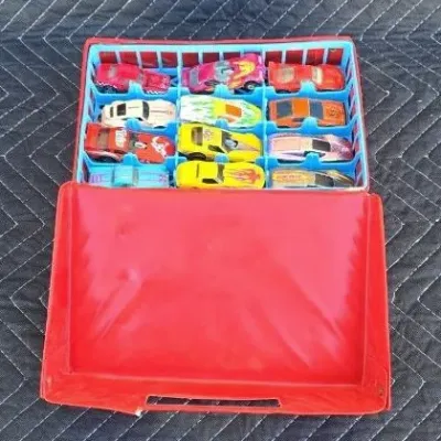 Vintage red vinyl toy car carrying case filled with various die-cast toy cars, including Hot Wheels and Matchbox models.