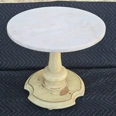 Vintage round side table featuring a white marble top on a distressed, cream-painted pedestal base with gold accents.
