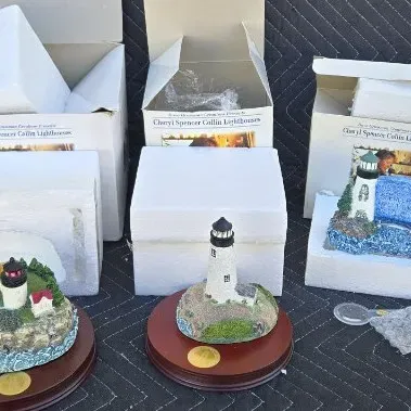 Three Cheryl Spencer Collin lighthouse figurines, including two with wooden display bases, shown with their original boxes and styrofoam...
