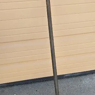 Vintage manual post hole digger with a T-handle and rusted metal blades, showing signs of heavy use.