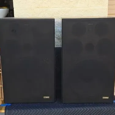 Pair of vintage Fisher floor-standing speakers with black fabric grilles and wood grain cabinets.