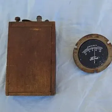 Vintage Ford Model T wooden ignition coil and a circular Ford amperes gauge, showing age-related wear and patina.