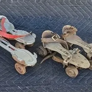 Two pairs of vintage metal clamp-on roller skates with leather straps, showing significant wear and rust consistent with age.