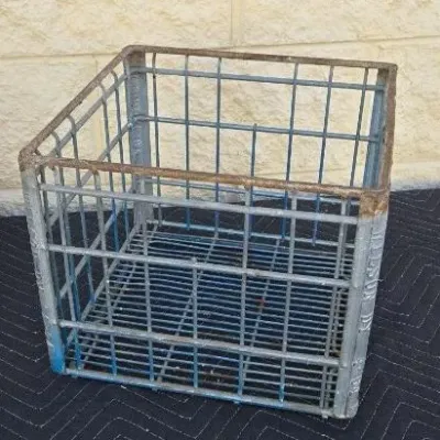 Vintage galvanized wire milk crate with blue paint remnants and surface rust, showing embossed lettering on the corner posts.