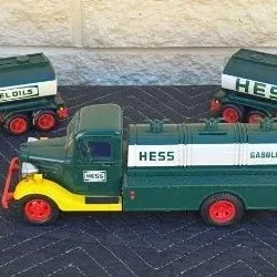 Three vintage Hess toy tanker trucks in classic green, yellow, and red livery, including two semi-truck models and one single-unit tanker.