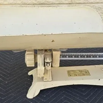 Vintage Detecto metal baby scale in off-white finish, featuring a curved tray and sliding weight mechanism.