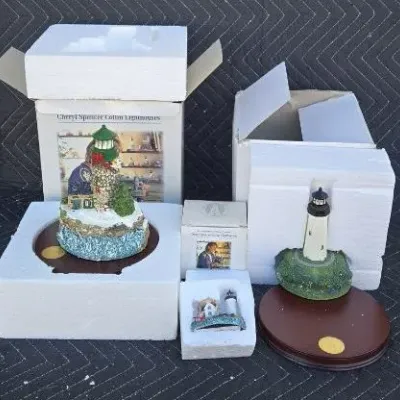 Three Cheryl Spencer Collin lighthouse figurines with their original boxes and styrofoam packaging, including a festive winter lighthouse...