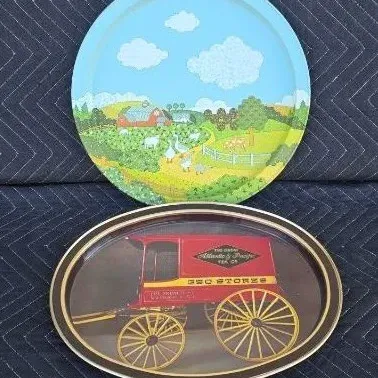 Two vintage metal serving trays, including a round tray with a colorful farm scene and an oval tray featuring a red Great Atlantic &...