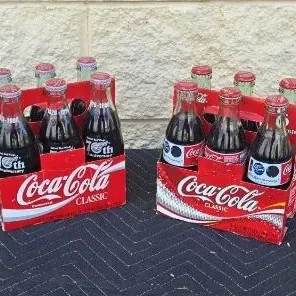 Two vintage six-packs of Coca-Cola Classic glass bottles in their original red cardboard carriers, featuring commemorative 75th...