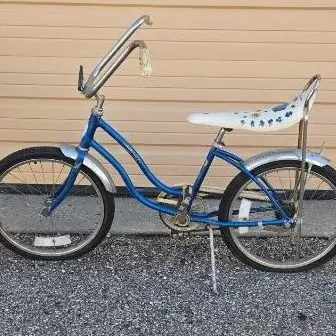 Vintage 1970s girls' banana seat bicycle in blue, featuring high-rise handlebars, chrome fenders, and a white floral-patterned...
