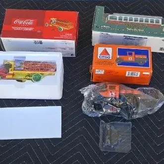 Collection of vintage collectible toy vehicles, including a Coca-Cola delivery truck, a Citgo truck, and a trolley car, some in their...