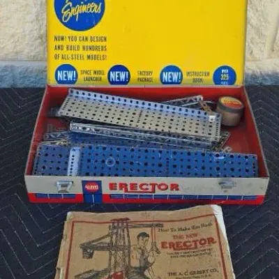 Vintage A.C. Gilbert Erector Set in its original yellow and red metal box, complete with metal building components and a worn instruction...