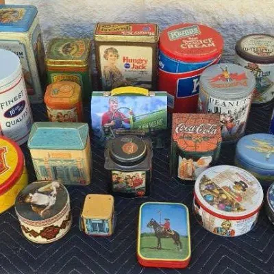 Collection of vintage advertising and decorative tins, featuring brands like Better Made, Coca-Cola, Hungry Jack, and John Deere.