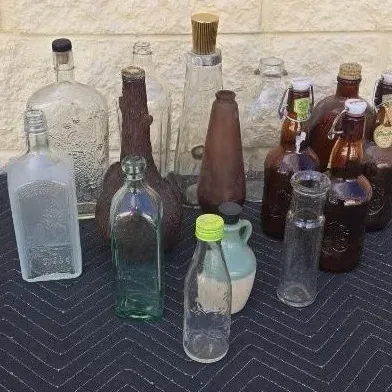 Collection of vintage glass bottles and jars in various shapes, sizes, and colors, including clear, amber, and green glass, along with a...
