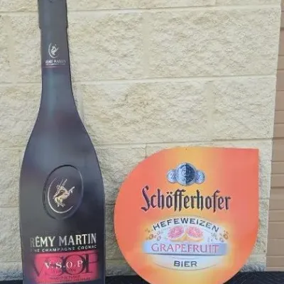 Vintage Rémy Martin VSOP bottle-shaped metal sign alongside a Schöfferhofer Grapefruit Hefeweizen Bier metal sign.