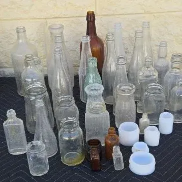 Collection of vintage glass bottles and jars in various sizes, shapes, and colors, including clear, amber, and light green glass.