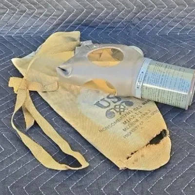 Vintage US military M1A2-1-1 noncombatant gas mask with attached canister filter and original canvas carrying bag.