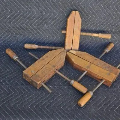 Three vintage wooden hand screw clamps, showing signs of age and use, displayed on a dark quilted moving blanket.