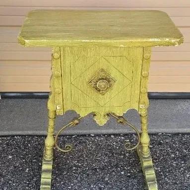 Vintage wooden side table painted in a distressed chartreuse green, featuring a single drawer with an ornate brass pull, turned legs, and...