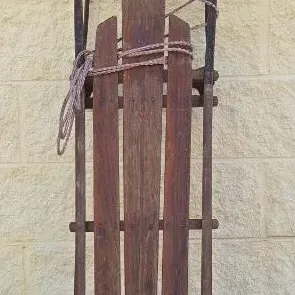 Vintage wooden flexible flyer sled with metal runners and steering bar, showing significant weathering and rustic patina.