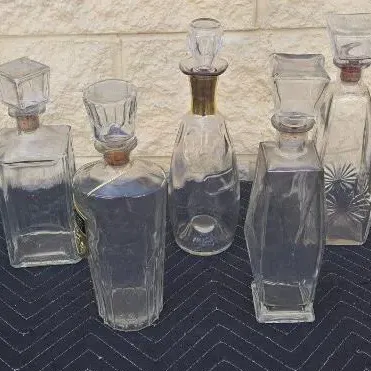 Collection of five vintage glass decanters in various shapes and sizes, featuring corked stoppers and decorative glass cuts.