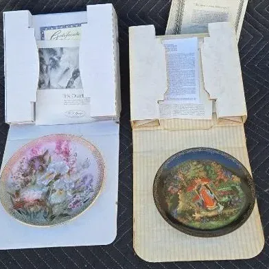 Two vintage collectible porcelain plates, including a floral iris design and a Russian fairy tale scene, both in their original cardboard...