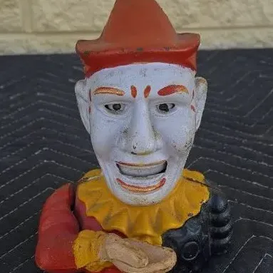Vintage cast iron mechanical bank featuring a clown bust with a red hat and yellow ruffled collar, showing some paint wear consistent...