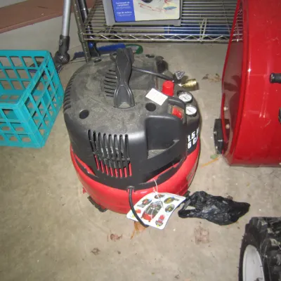 Portable pancake air compressor with a red tank and black motor housing, showing some dust from storage.