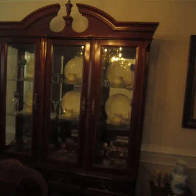 Traditional mahogany china cabinet featuring a broken pediment top with a central finial, glass display doors, and interior shelving...