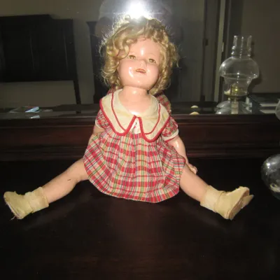 Vintage Shirley Temple composition doll, circa 1930s, wearing a red and green plaid dress with a white collar, showing some age-related...