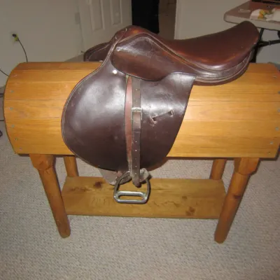 Vintage English leather riding saddle with stirrups, displayed on a custom wooden saddle stand.