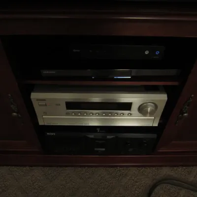 Onkyo silver-faced AV receiver and a Sony component housed inside a dark wood media console.