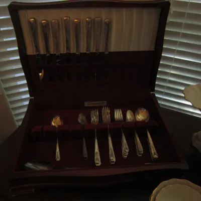 Vintage silverware set housed in a dark wood storage chest with a red velvet-lined interior.
