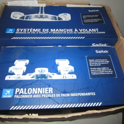 Saitek Pro Flight Yoke System and Pro Flight Rudder Pedals, both in their original blue retail boxes and stored inside a cardboard...
