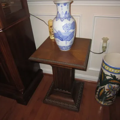 Traditional wooden pedestal side table with a fluted column base, displaying a blue and white ceramic vase with floral motifs.